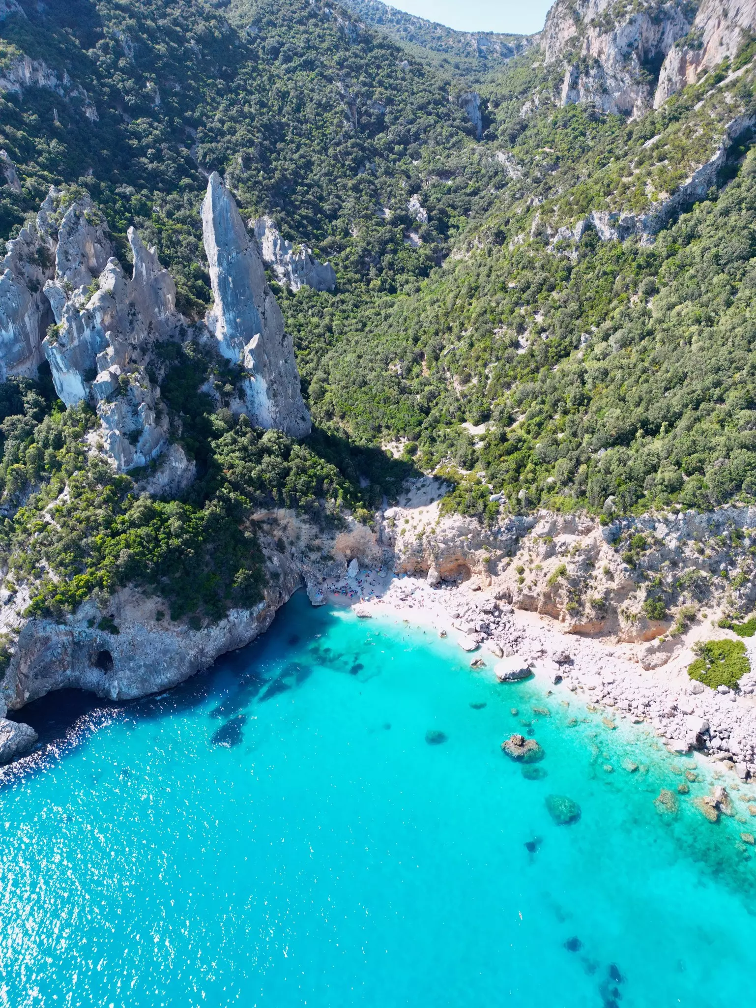 The strikingly blue ocean off a sandy beach backed by rocky cliffs on a sunny warm day in Sardinia. 