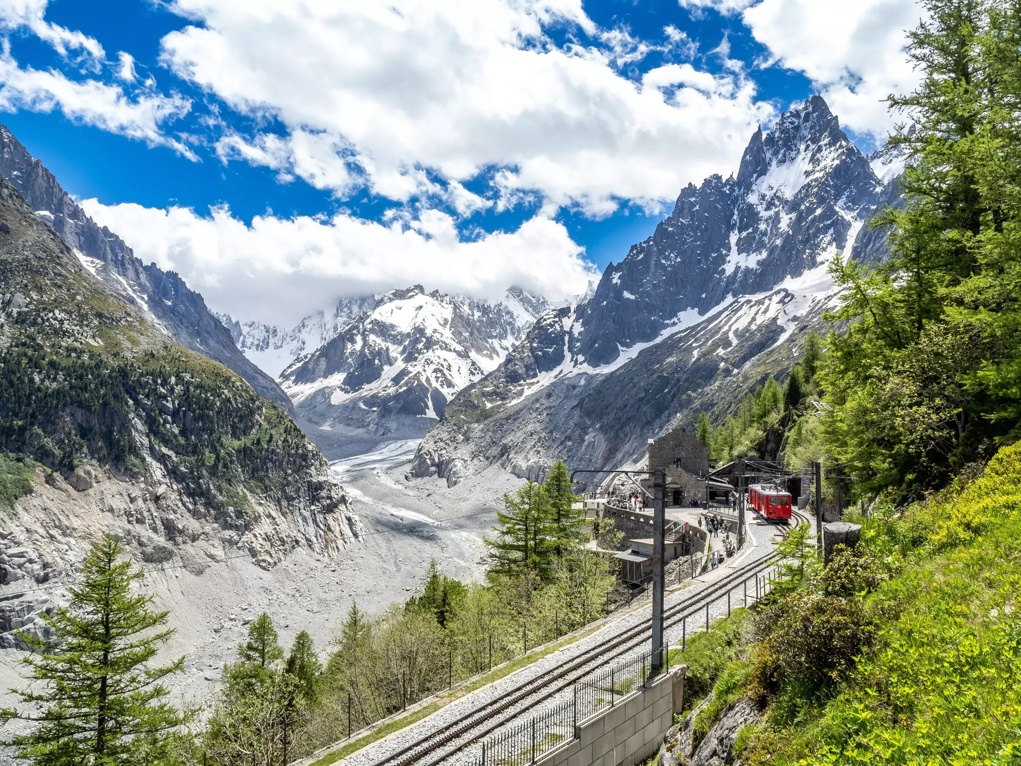 A vast glacier in a mountain valley. A red train passes nearby on a mountain railway track. 