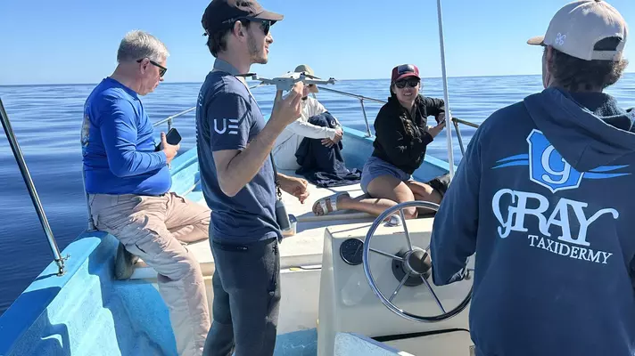 Dan from Uncharted Expeditions with navy shirt holding a drone on a boat.