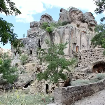 Weathered rock pinnacles with small wooden doors and windows above dry-stone walls, trees and a stone stairway