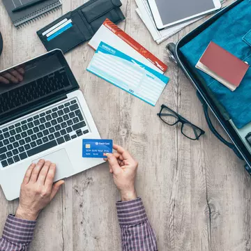 Traveler getting ready for a trip, he is packing his bag and booking a flight online using a credit card and a laptop, flat lay  License Type: media  Download Time: 2023-04-28T13:53:26.000Z  User:   Is Editorial: No  purchase_order:   