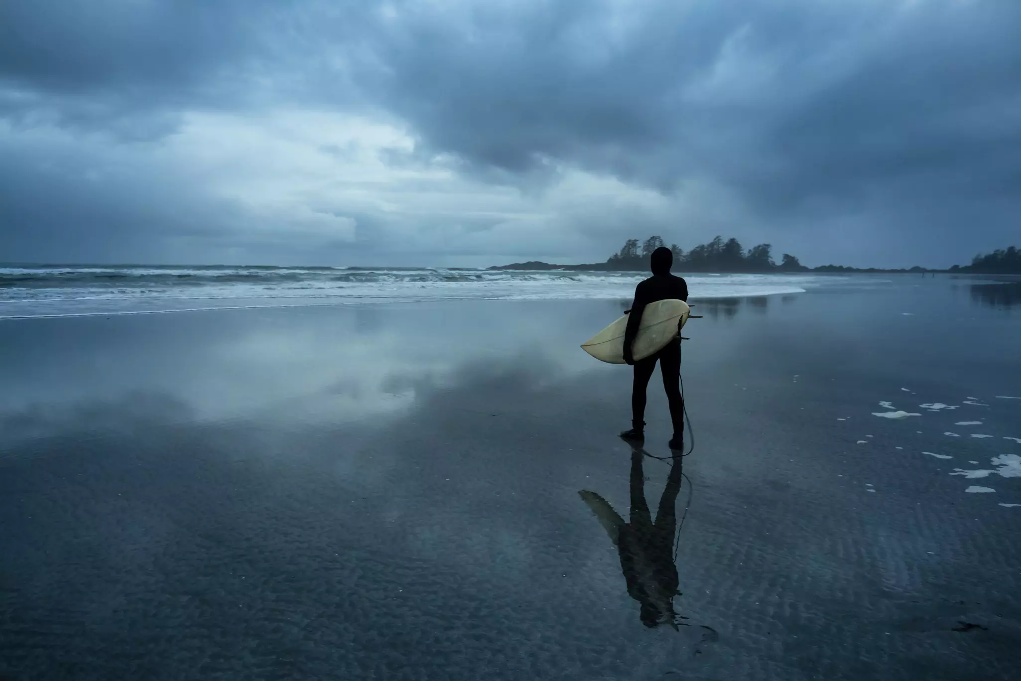 Surfer heading out in the ocean during a cloudy winter sunset