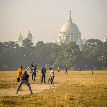 A cricket match in Maidan with the Victoria Memorial in the distance. Kolkata, West Bengal, India.
