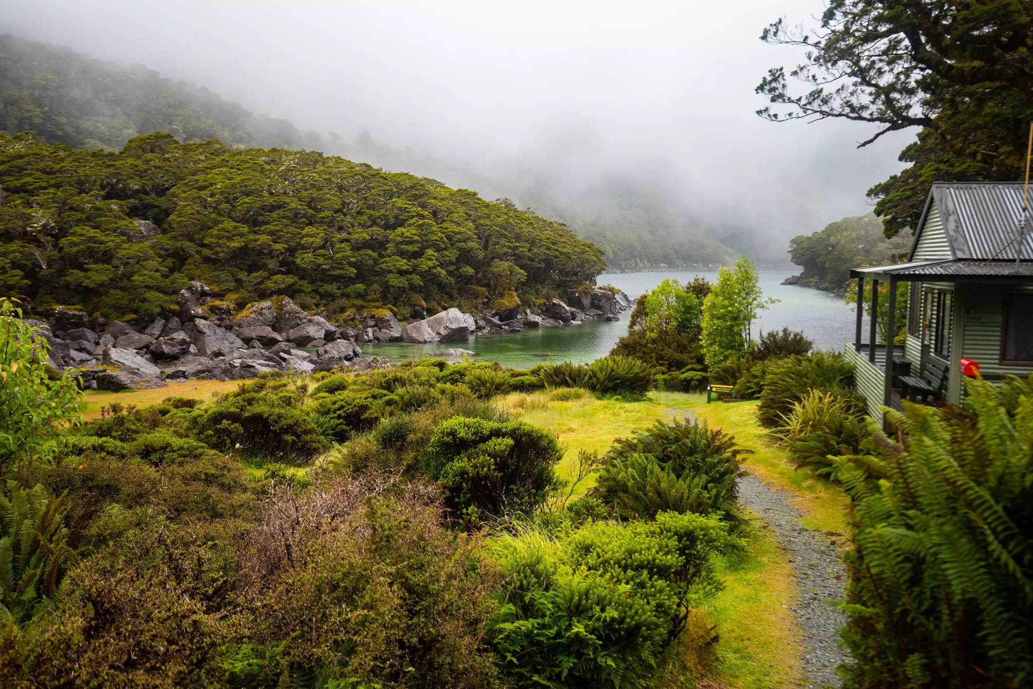 A lakeside hut near a hiking path, with mist and clouds rolling in off the water.