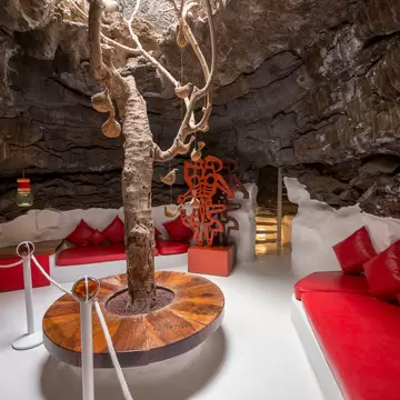 Red leather banquettes curve around a tree trunk growing up through a rough black lava ceiling