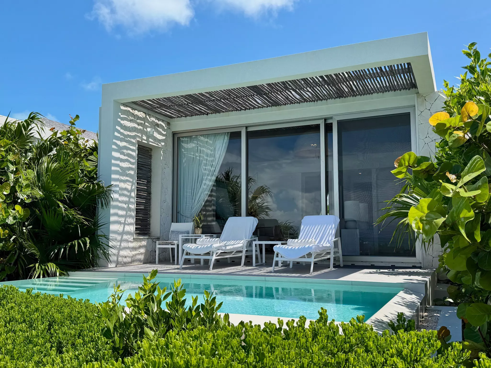 Two sunloungers sit on a deck between a hotel suite and a plunge pool