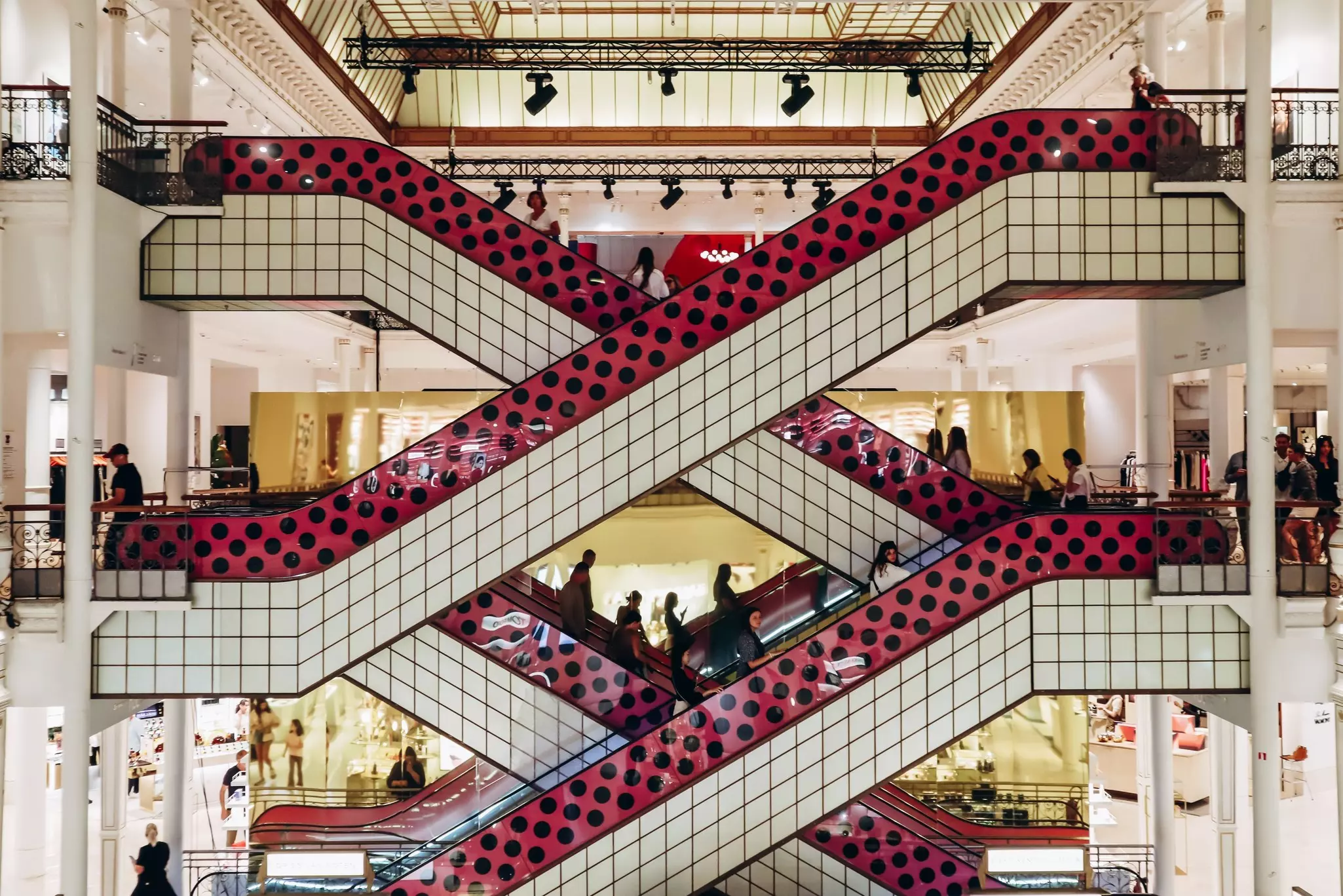 Crisscrossing escalators in a department store are covered in white and polka-dot tiles.