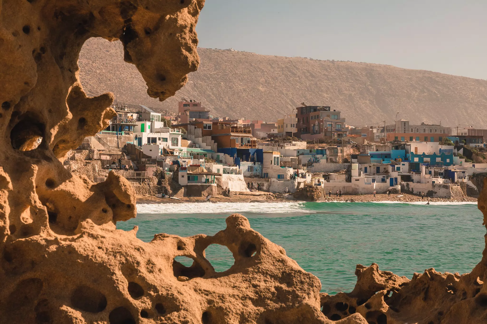 View of a Moroccan fishing village with the rocky terrain and ocean in the foreground, and a cliff in the background