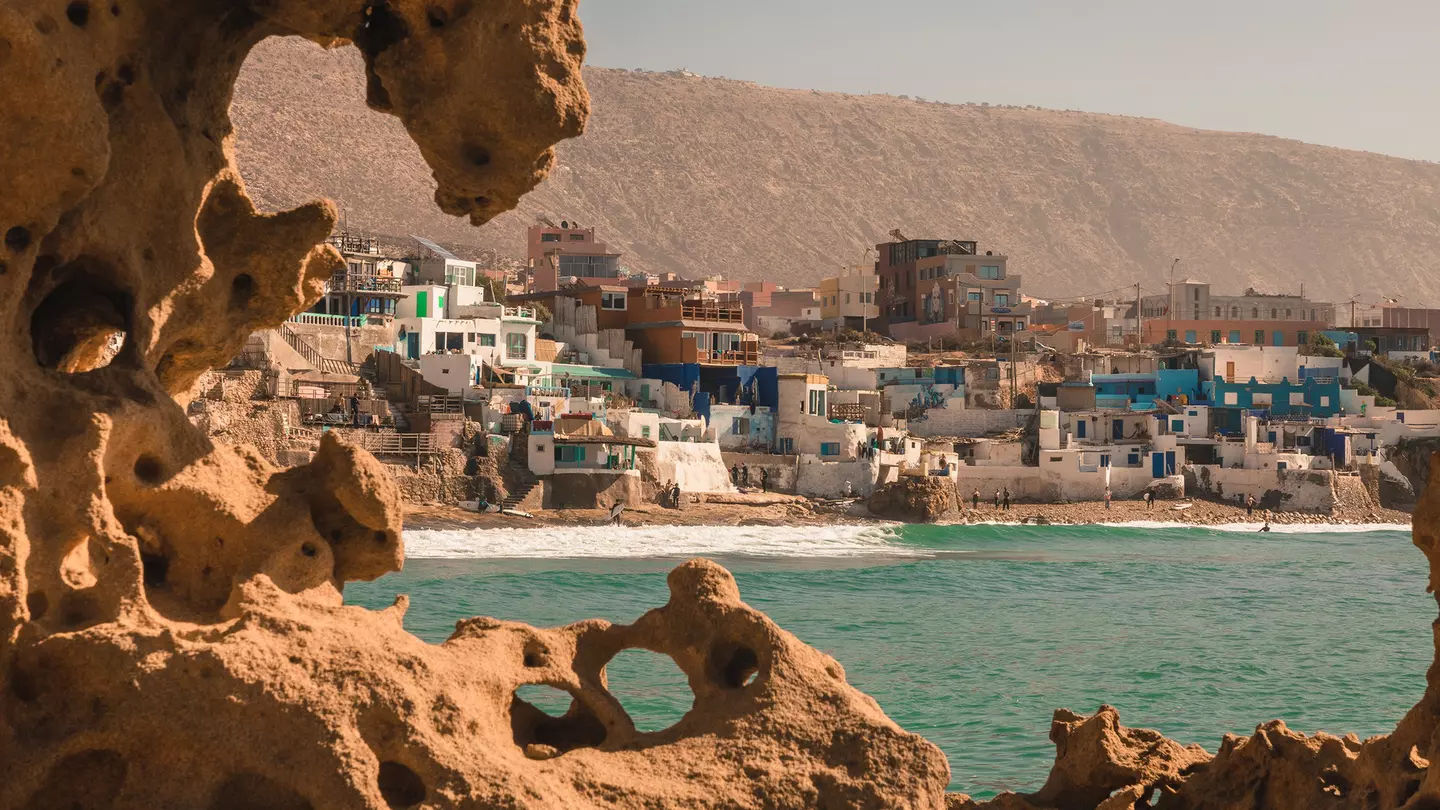 View of a Moroccan fishing village with the rocky terrain and ocean in the foreground, and a cliff in the background