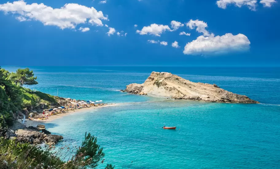 Kefallonia coast near Argostoli: sunshades on a pine-backed beach facing a pale rock islet in turquoise sea