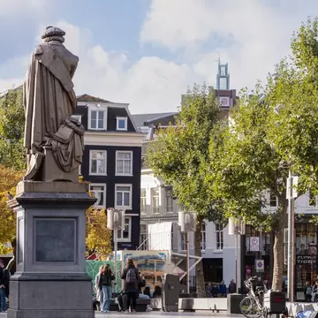 People enjoying the sunny autumn weather at the famous Rembrandtplein in Amsterdam, with a statue in the foreground.