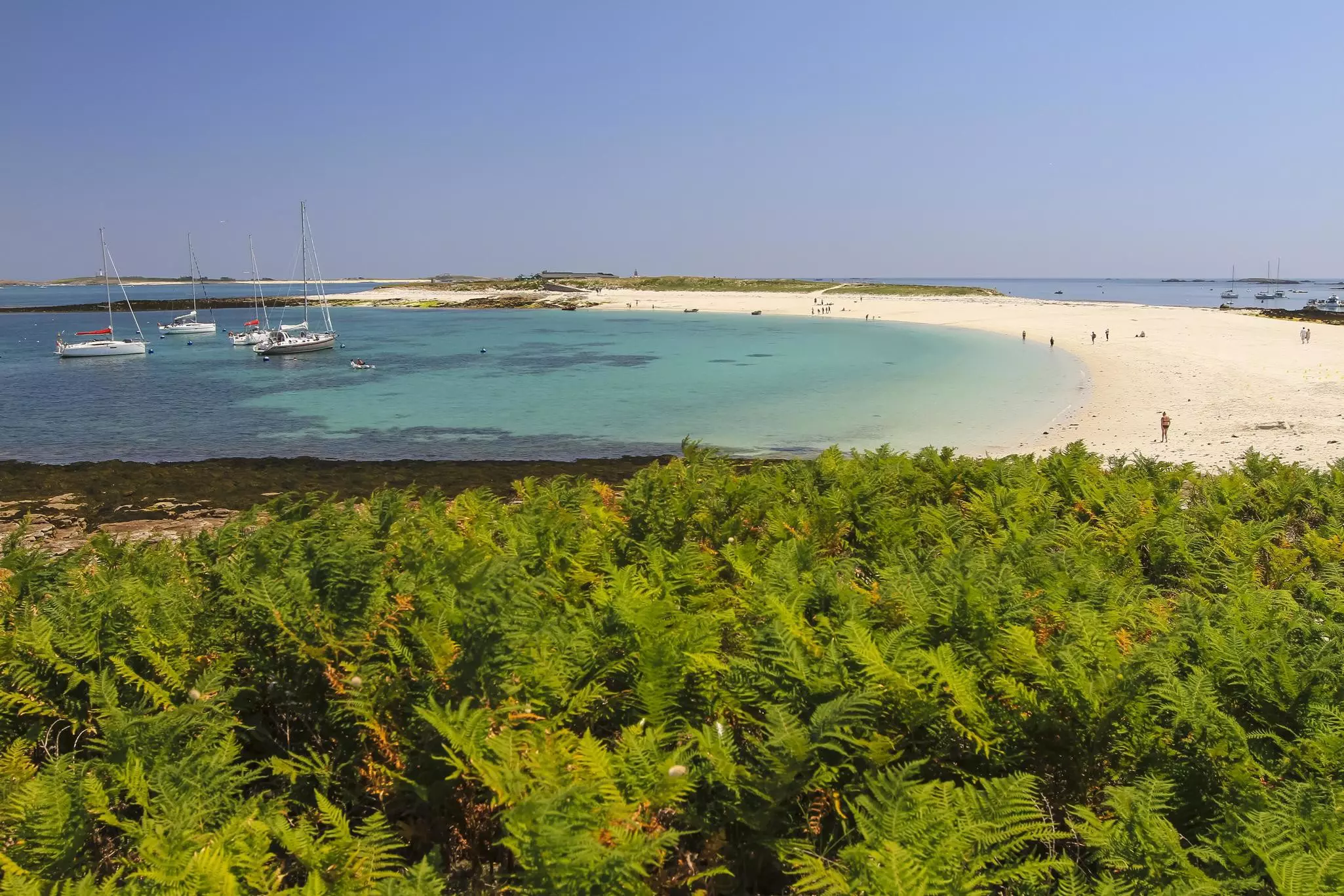 A few sailing boats docked in the shallows off a wide arc of golden sand.