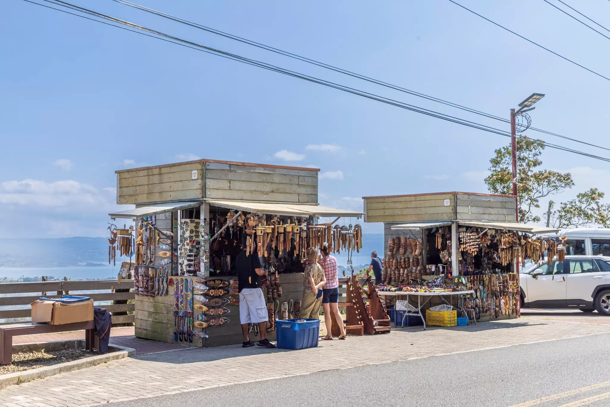 A row of stalls beside a road near a lake selling wooden trinkets and souvenirs.