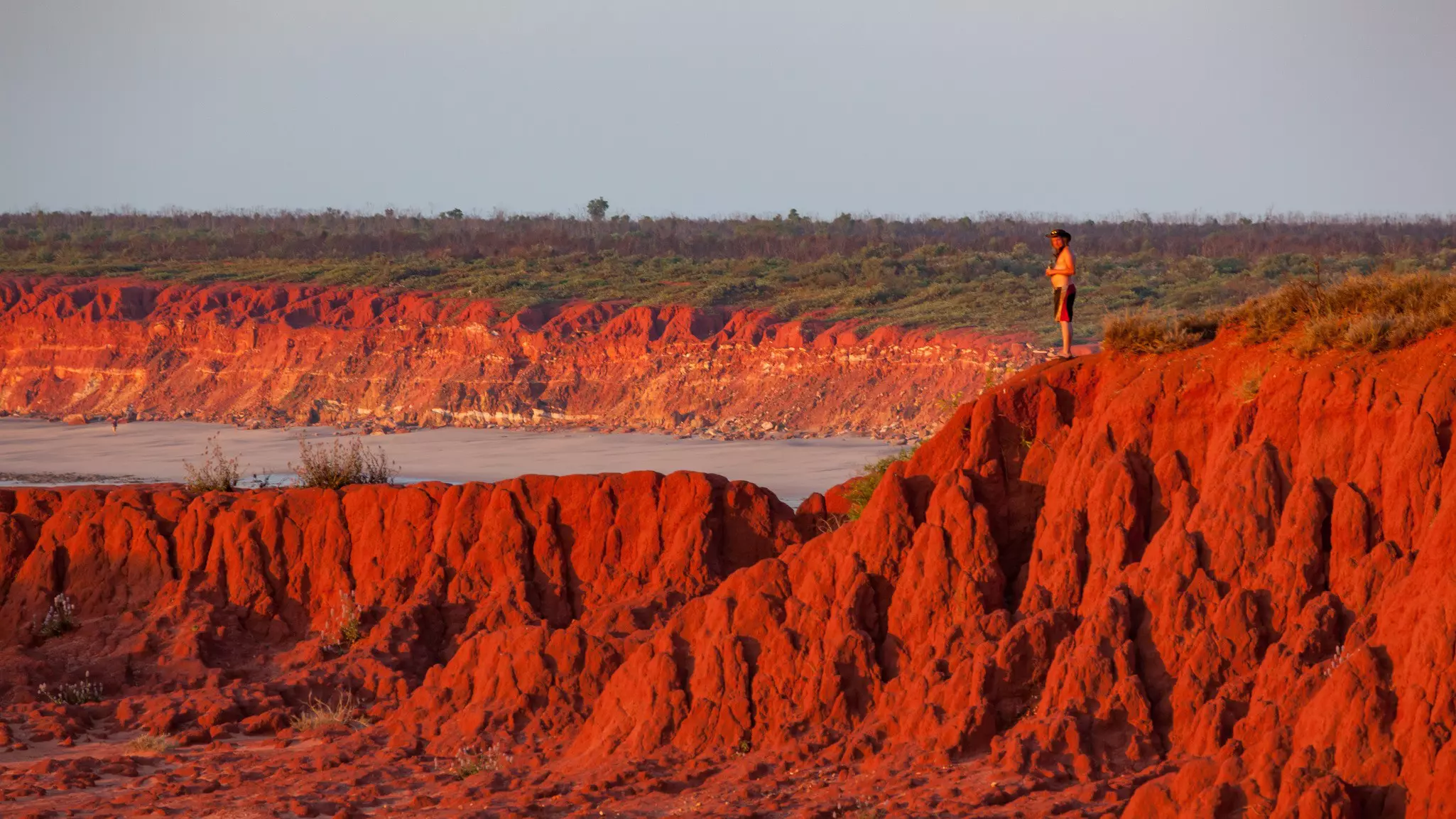 Man standing on top of the Red Pindan Cliffs at sunset, James Price Point, Western Australia.