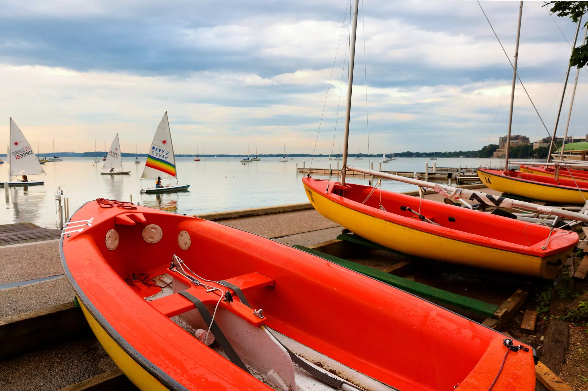 Small sailing boats in a lake and some docked on a cement platform.