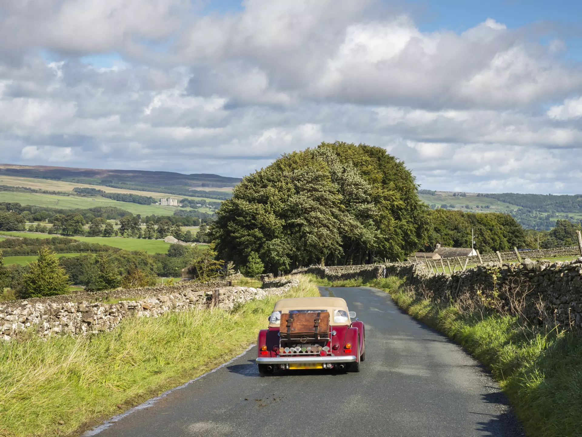 Little red car driving near Aysgarth in the Yorkshire Dales on a sunny September day. Bolton castle seen in the far distance.
850110370