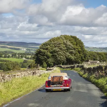 Little red car driving near Aysgarth in the Yorkshire Dales on a sunny September day. Bolton castle seen in the far distance.
850110370