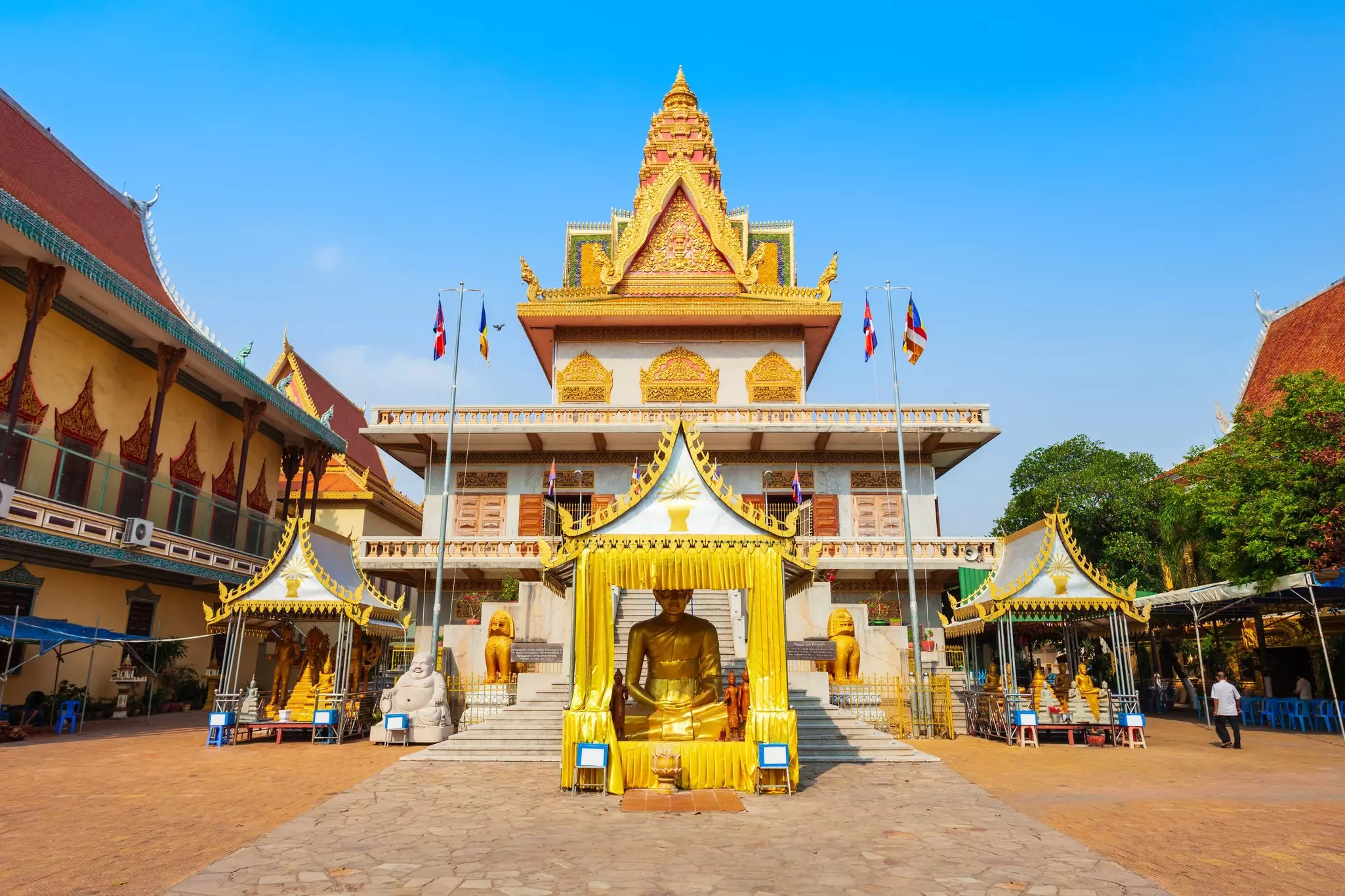 A white temple with gold trim with a gold Buddha statue in front