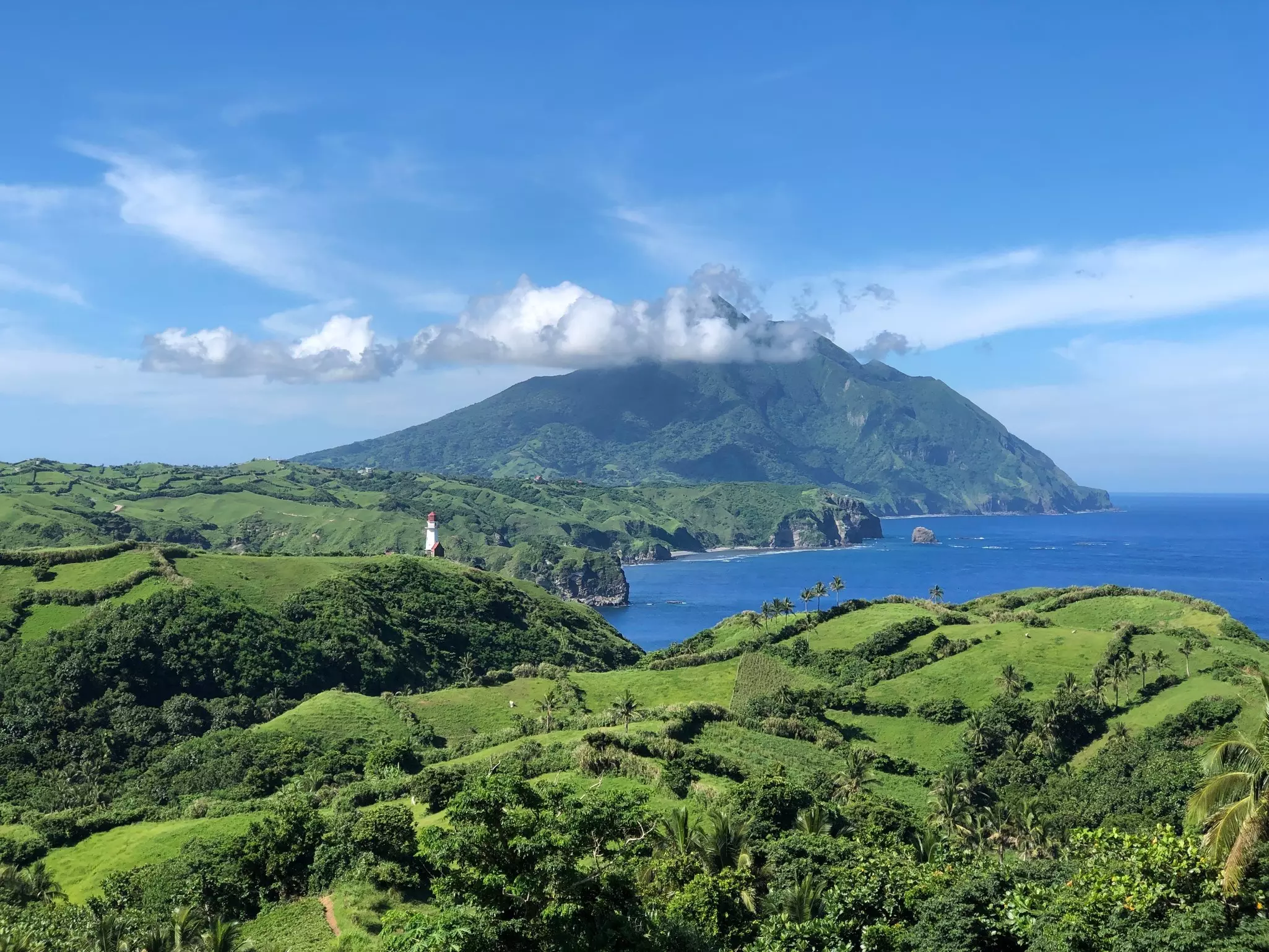 Green rolling coastal hills with a tall white lighthouse.