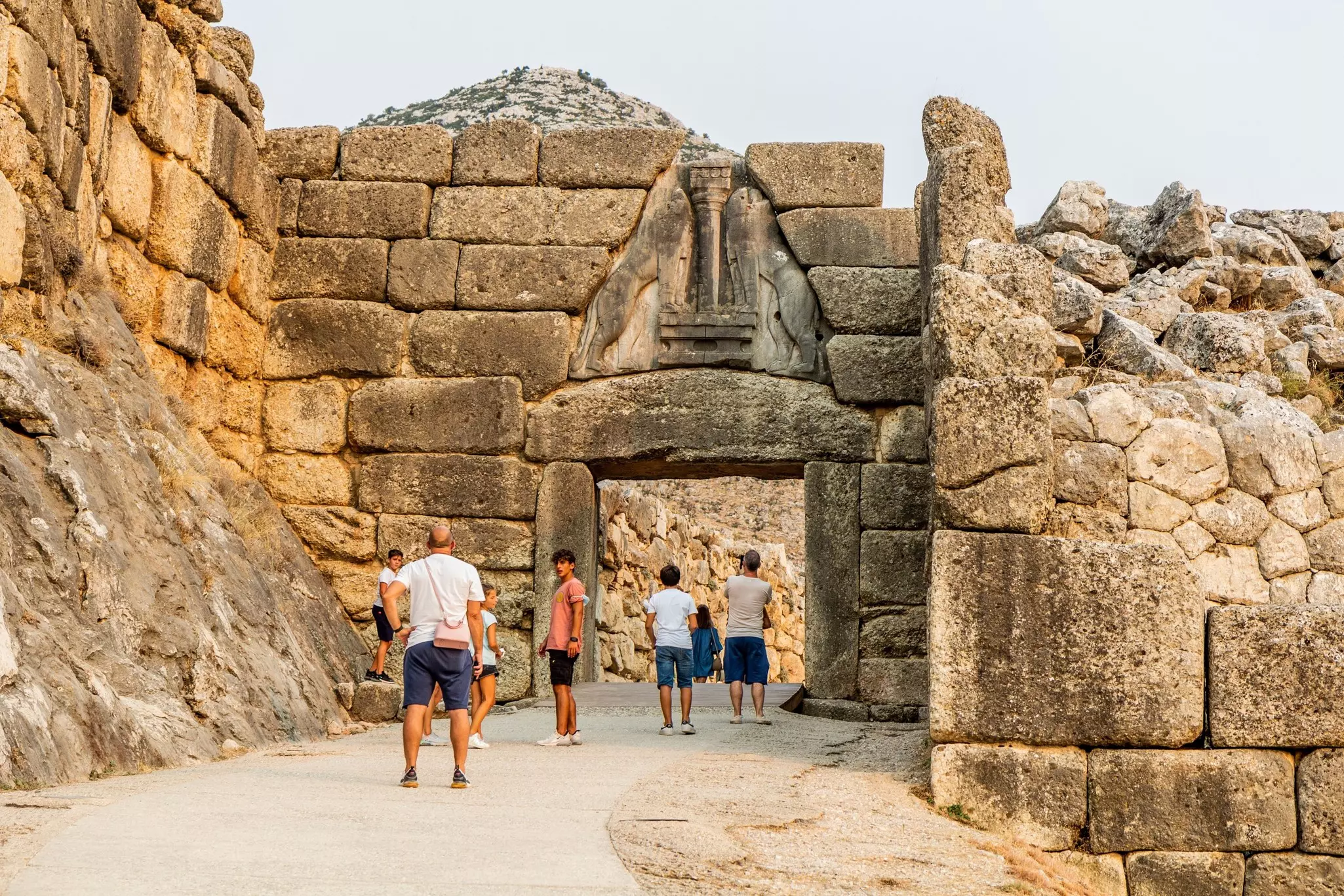 People stand near and under a massive portal made of stones at an ancient citadel.