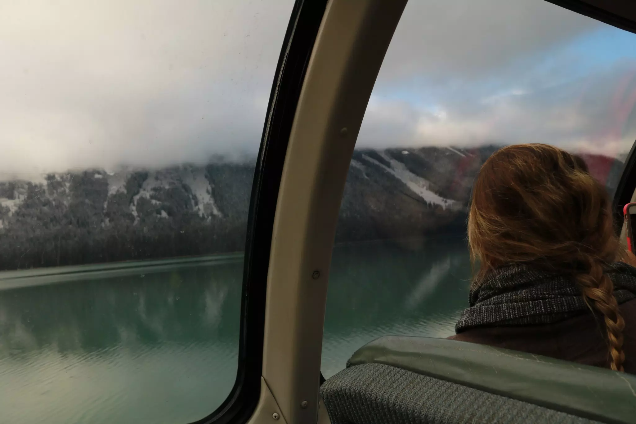 Woman looking through window at fog-covered mountains from inside a glass-domed train car.
