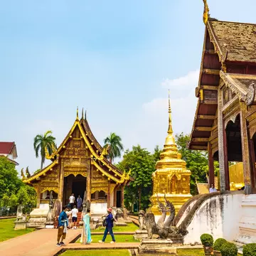 People walk around the grounds of a temple complex with golden features on its buildings and shrines.