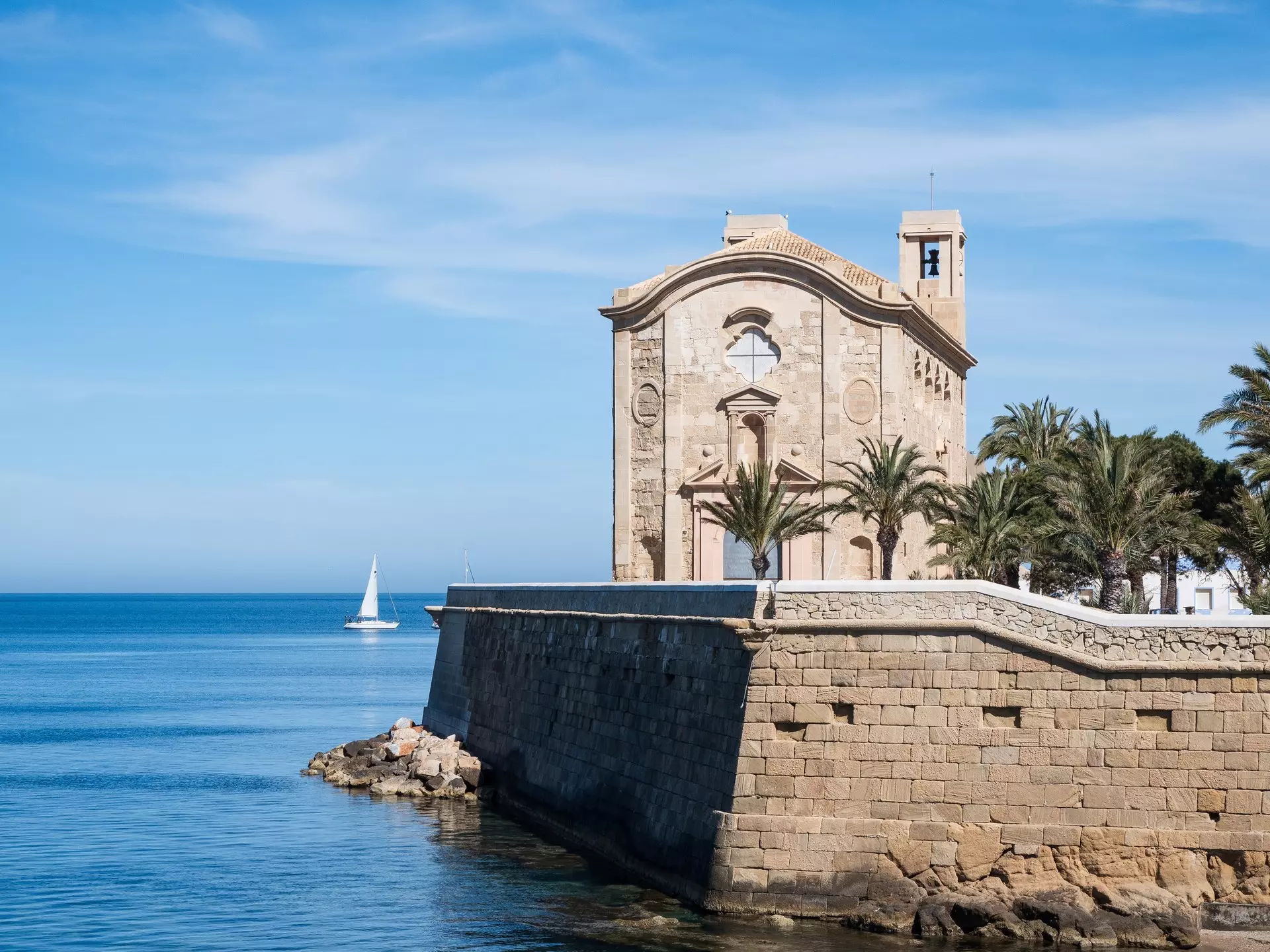 A sailboat passes a historic stone church.