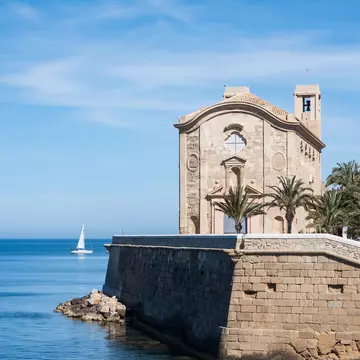 A sailboat passes a historic stone church.