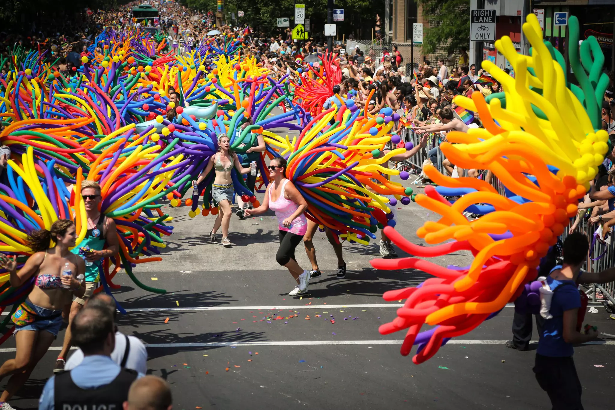 Revelers with many colorful long, thin balloons attached to their backs dance and run during a street parade