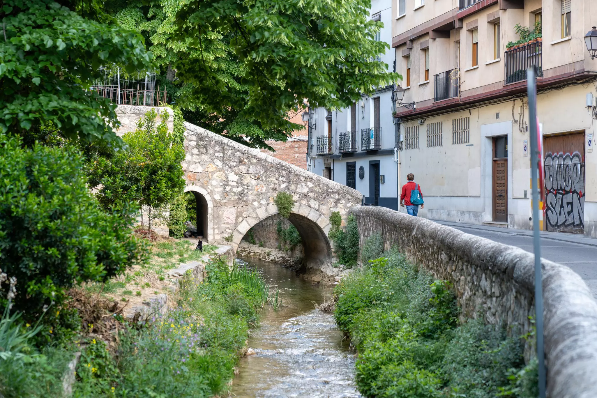 A man walks by a river inside the The Walled City of Cuenca.