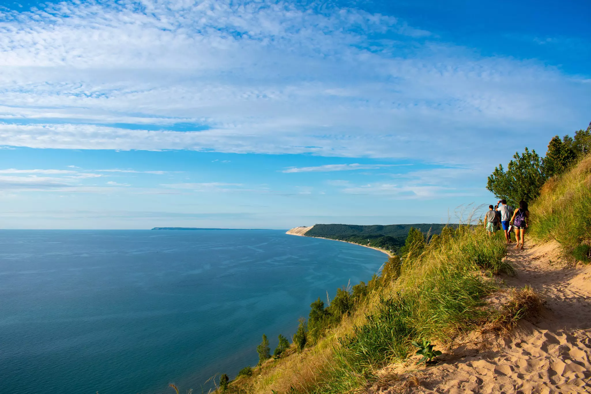 Four people follow a sandy coastal cliff path on a sunny day with the ocean stretching out in the distance.