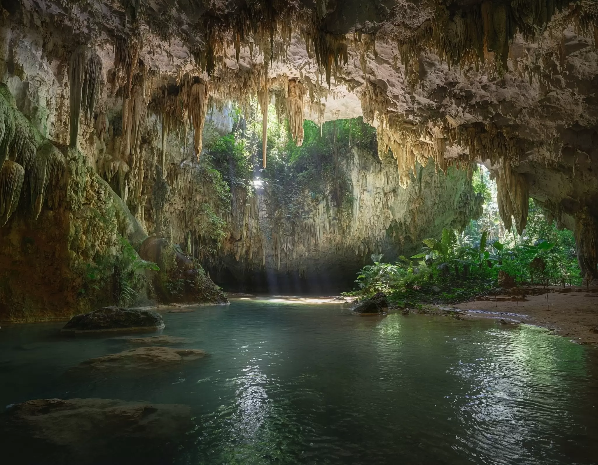 Sunlight glows though an opening in stalactites over an underground body of water