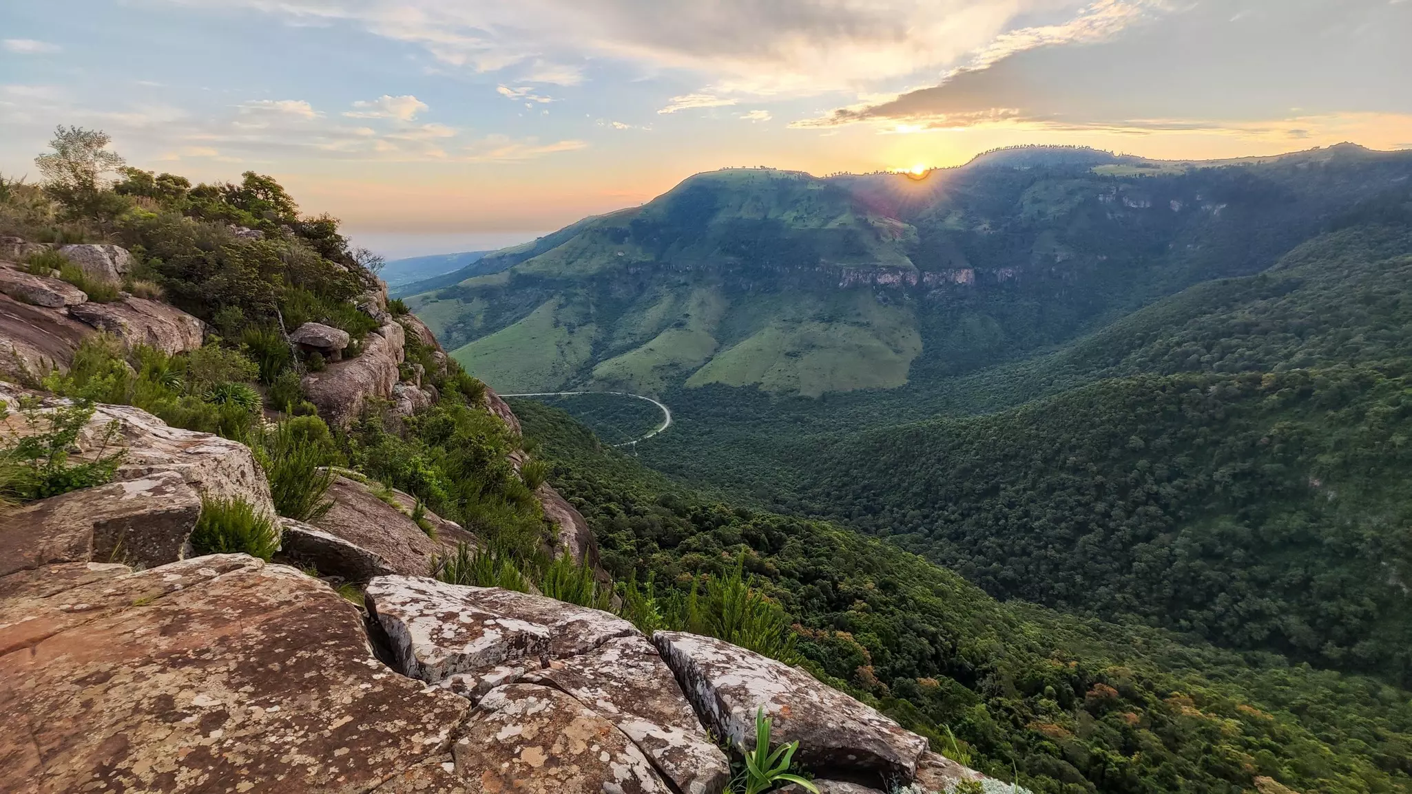 A rocky viewpoint above rolling countryside at sunset.