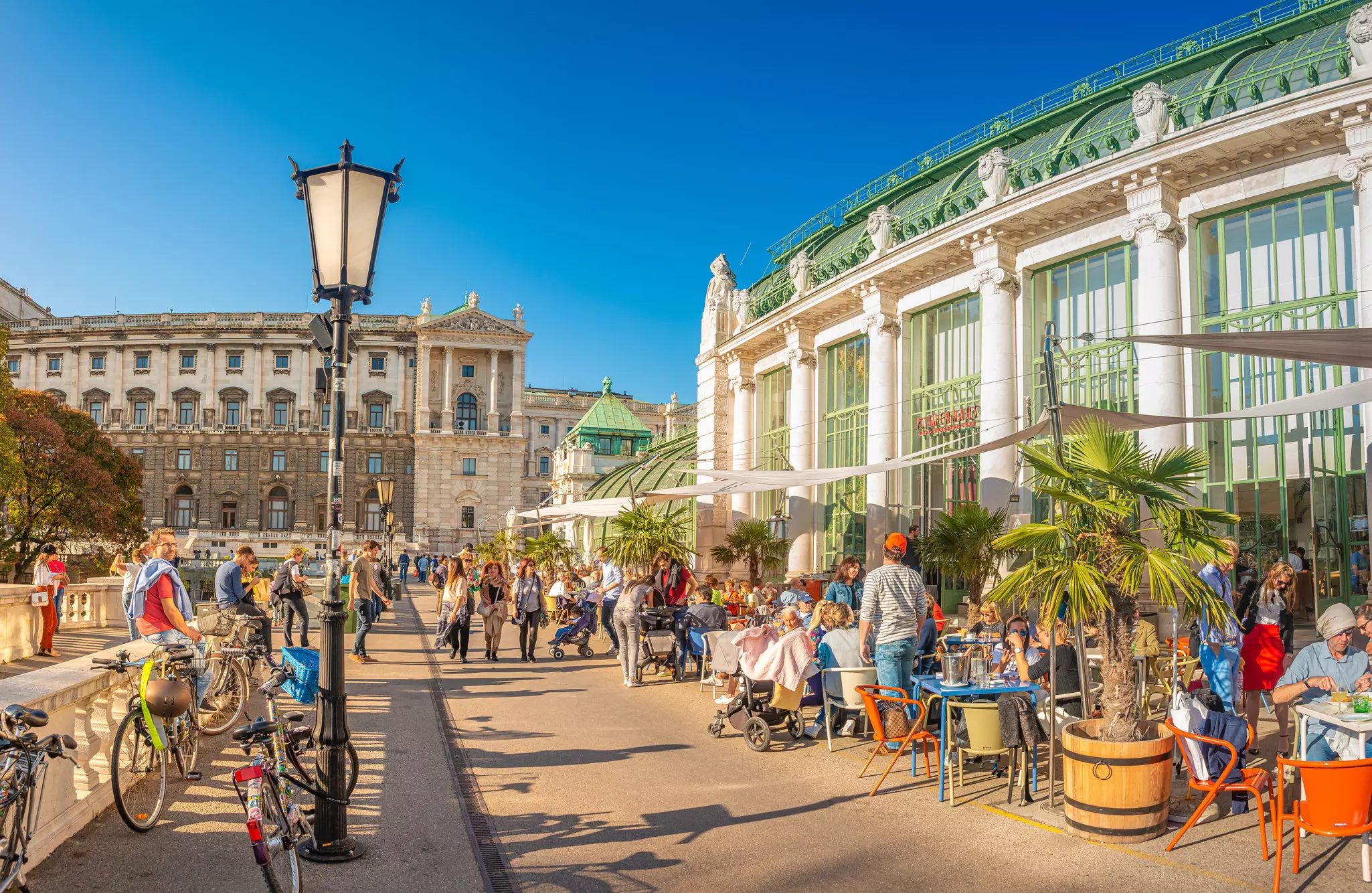 People sit at cafe tables outside a large conservatory cafe on a sunny day