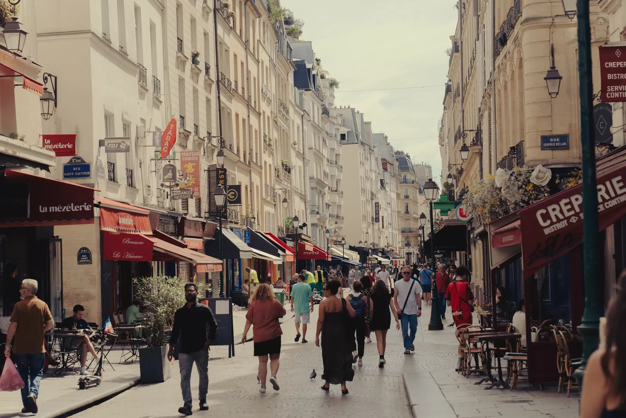 People walk down a road in Paris lined with shops and restaurants and traditional French architecture