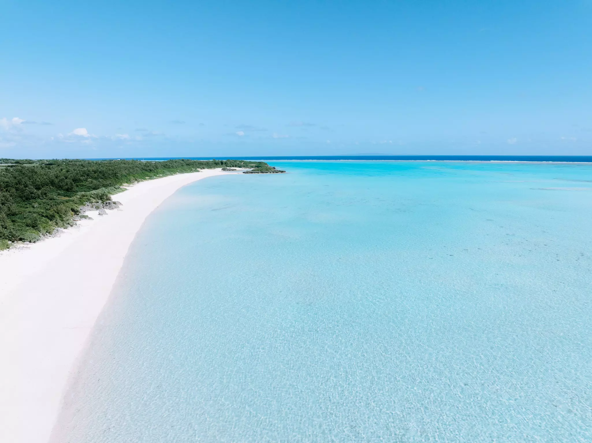 A long stretch of white sand on a tropical beach lapped by clear waters in a coral-reef lagoon.
