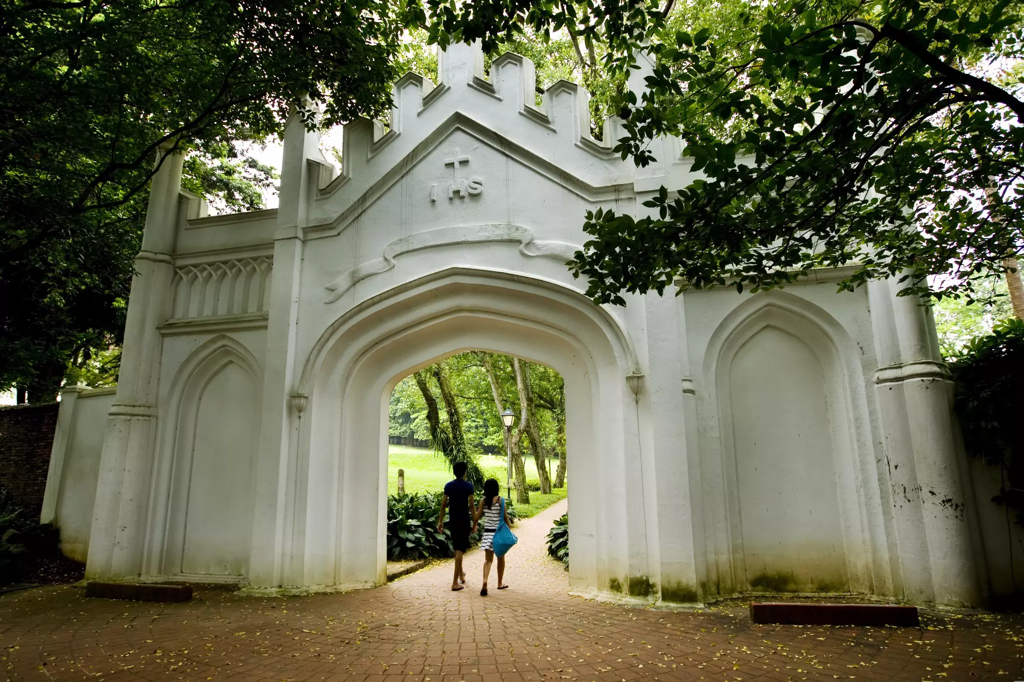 Two people walk through an enormous Gothic-style gate in a park
