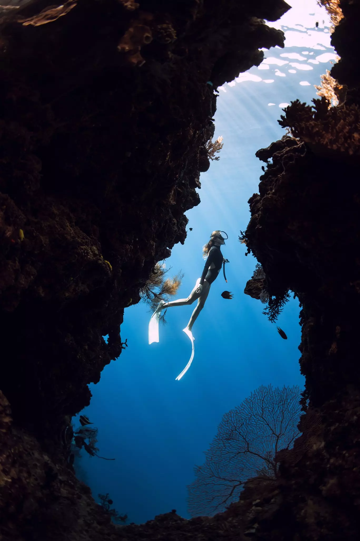 A diver with long fins on her feet is framed in the opening to an underwater cave.