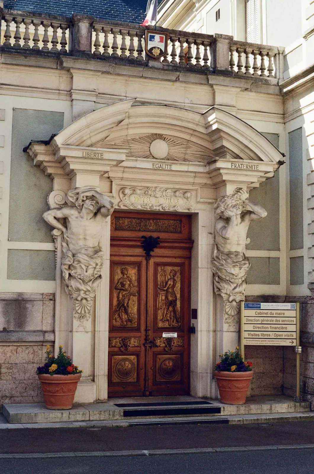 The large carved wooden and gold door of Villa Lumière, today's town hall in Évian-les-Bains, France. The archway around the door has carvings of two people and reads "Liberte, egalite, fraternite"
