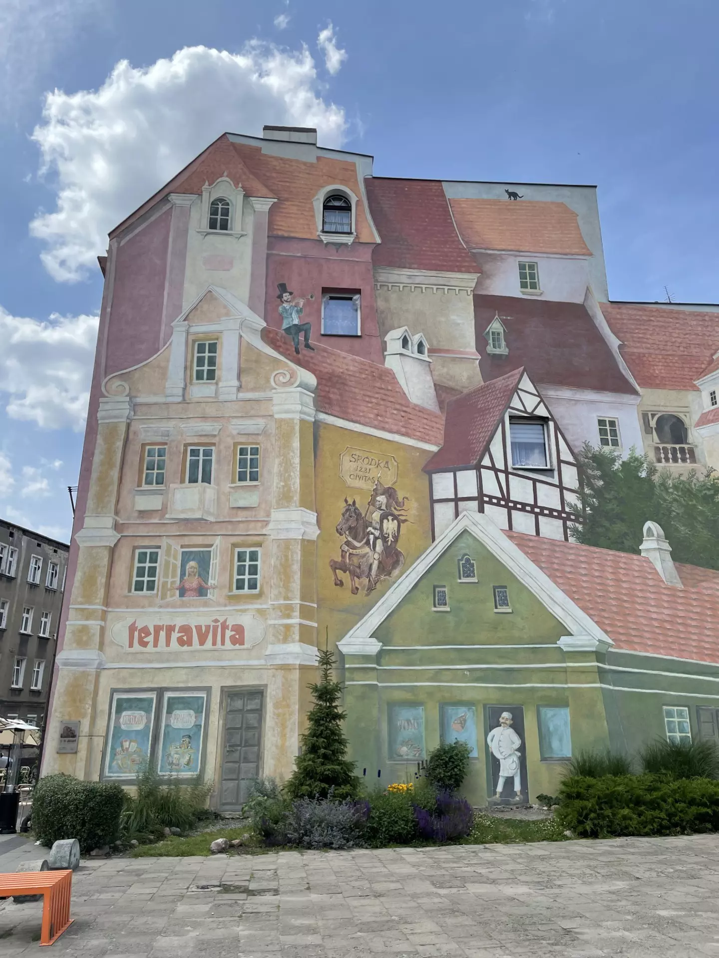 Mural painted on the side of a building that depicts a man sitting on a roof, a cat standing on another roof, and a man standing in a doorway.