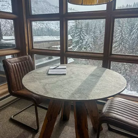 A journal and two chairs in front of a window with views of snowy trees.  
