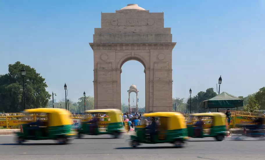 India Gate war memorial arch with blurred green and yellow auto-rickshaws passing in front, New Delhi, India