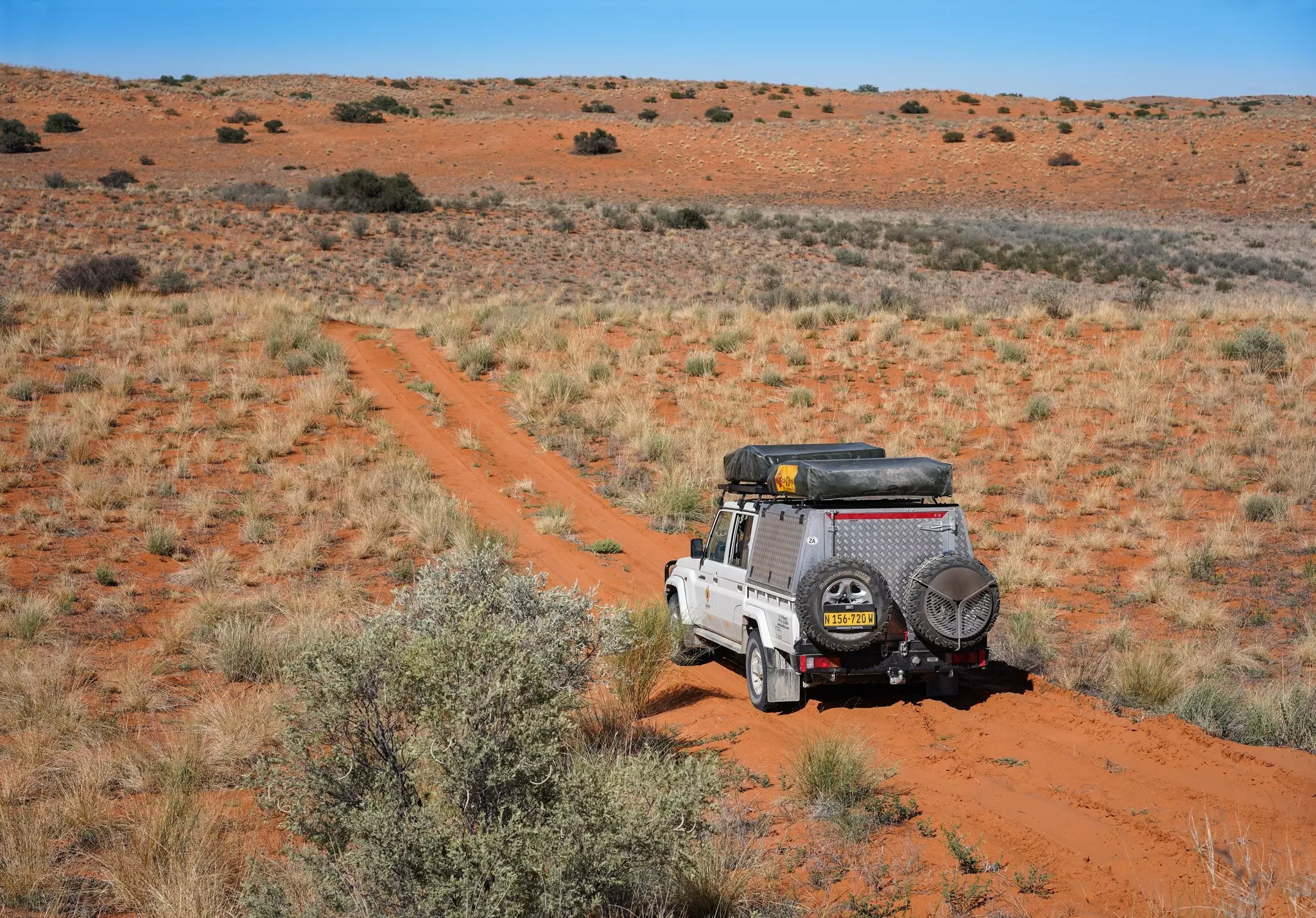 A four-wheel drive truck drives along a dusty red-sand path in a desert environment.