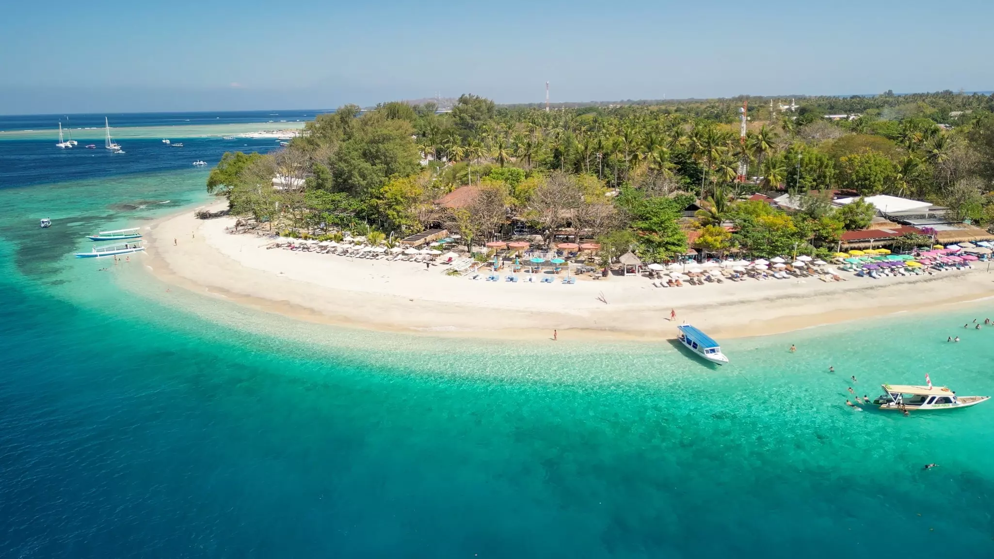An aerial view of a curved tropical beach with shallow blue-green water.