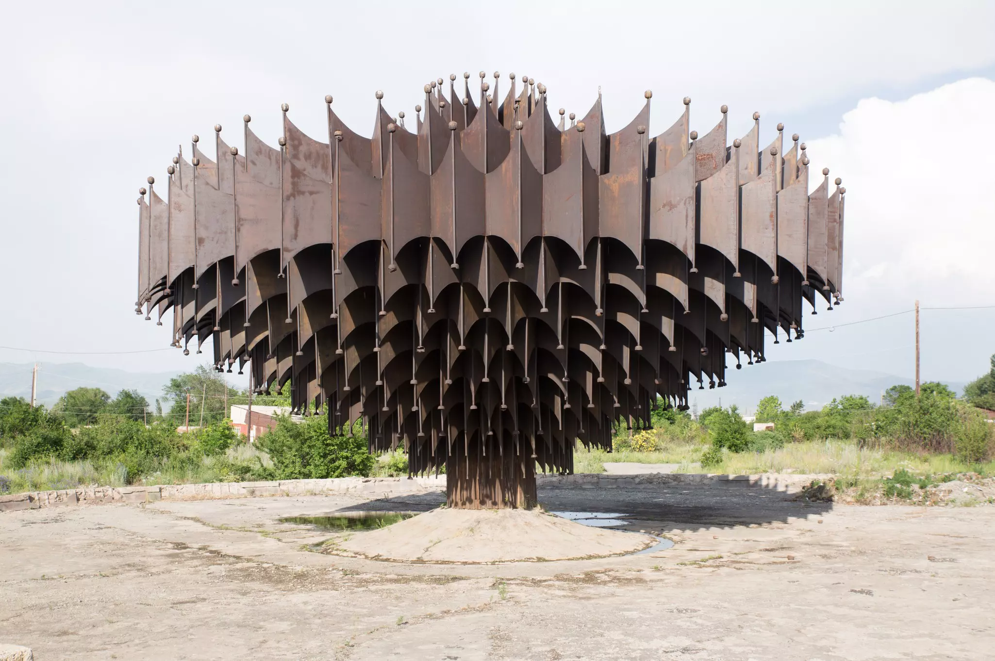 A large, spiky, conelike rusted iron structure rising from dry ground