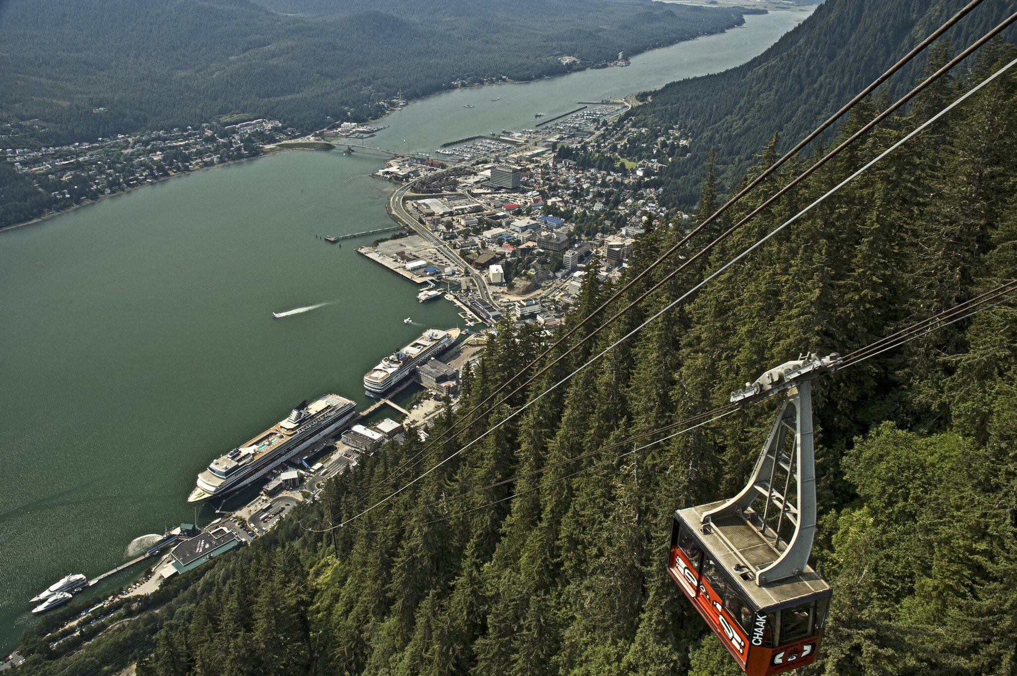 A large gondola over a waterway and a cliff covered in dense forest.