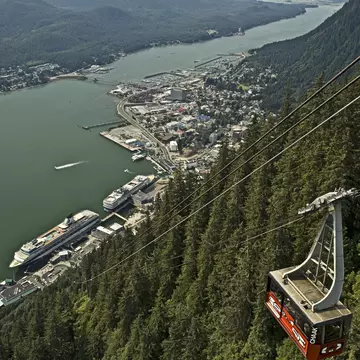 A large gondola over a waterway and a cliff covered in dense forest.