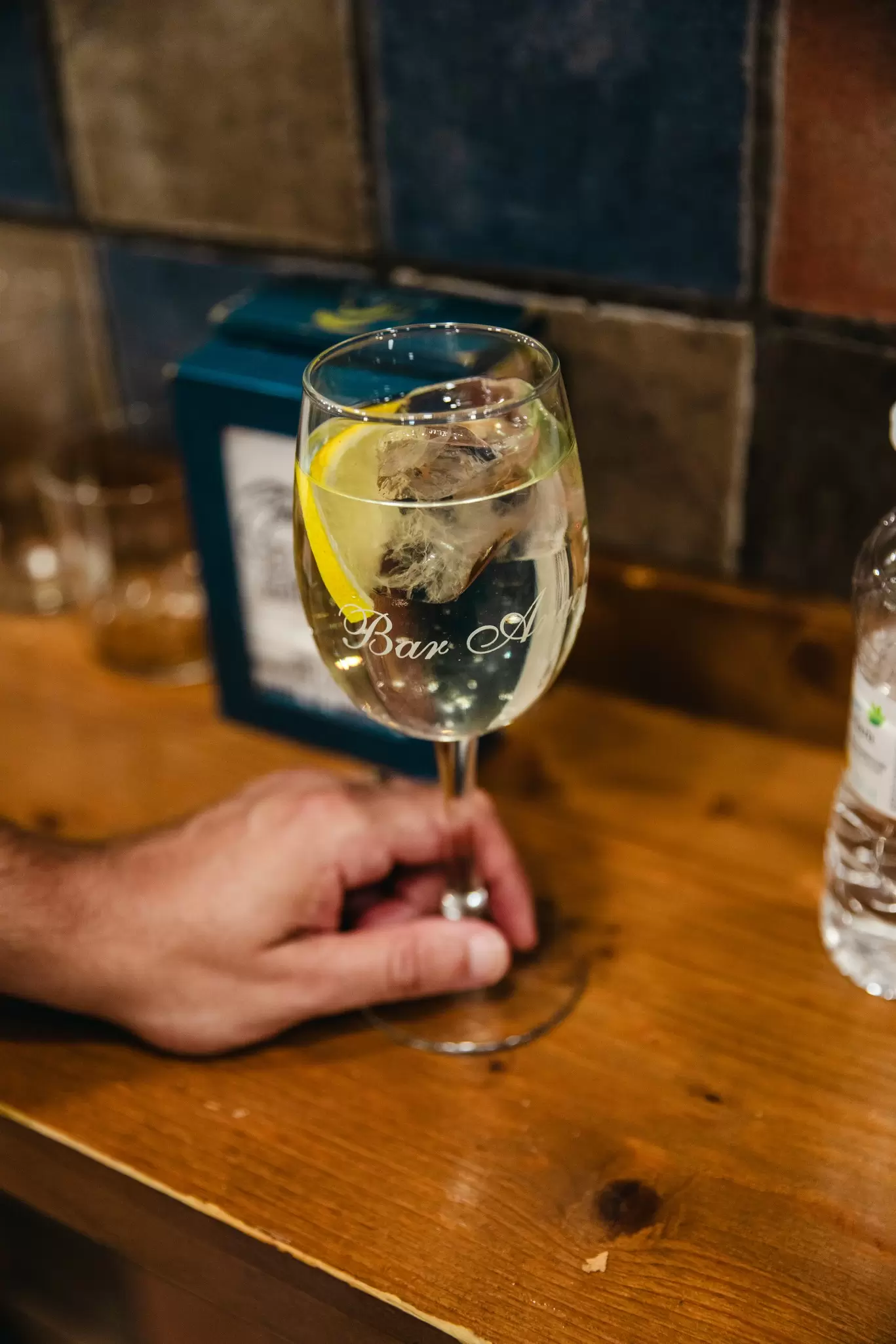 A hand holds a white vermouth in a glass with the words "Bar Ángel" etched on it