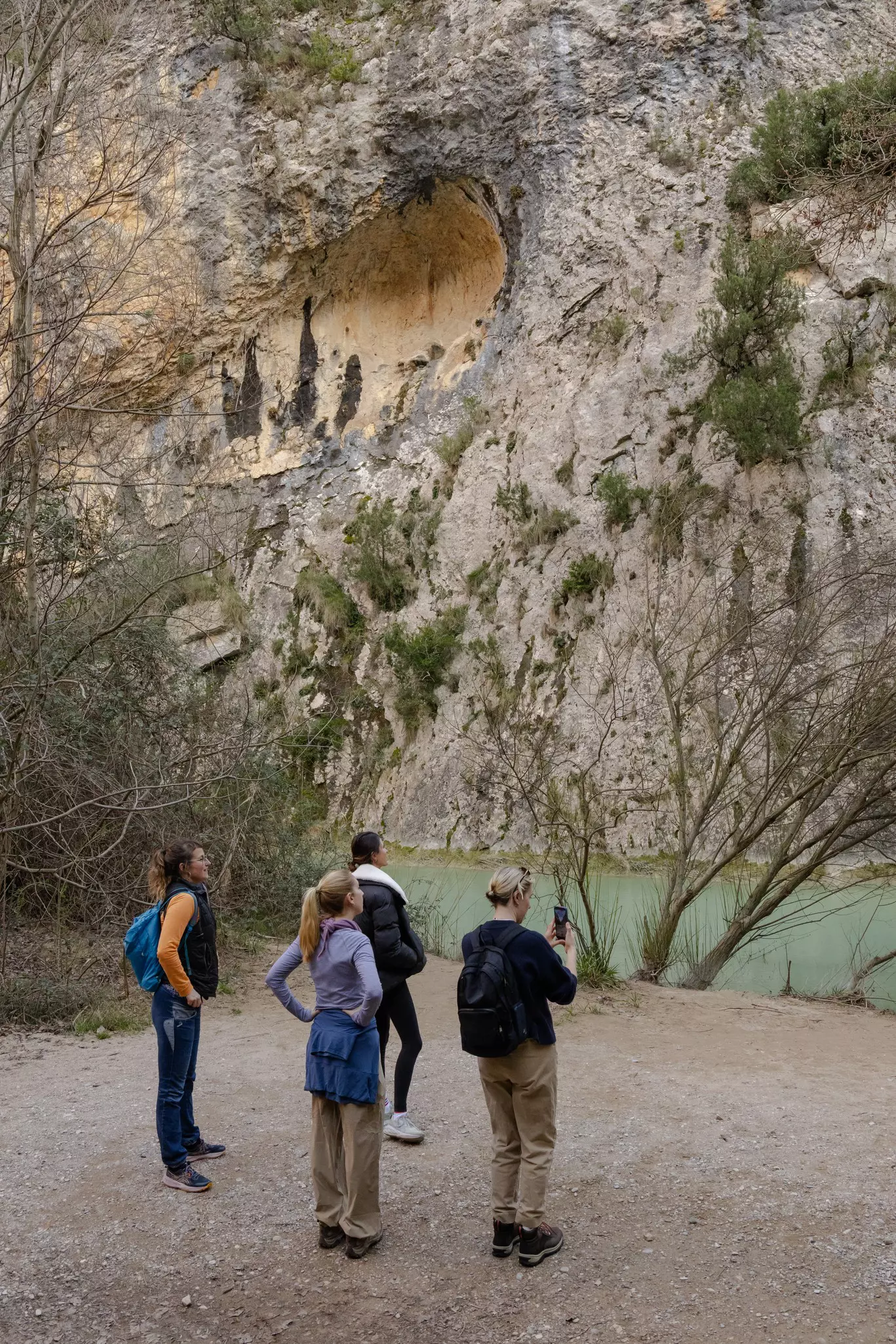 Four hikers pause on a trail beside a river running through a gorge.
