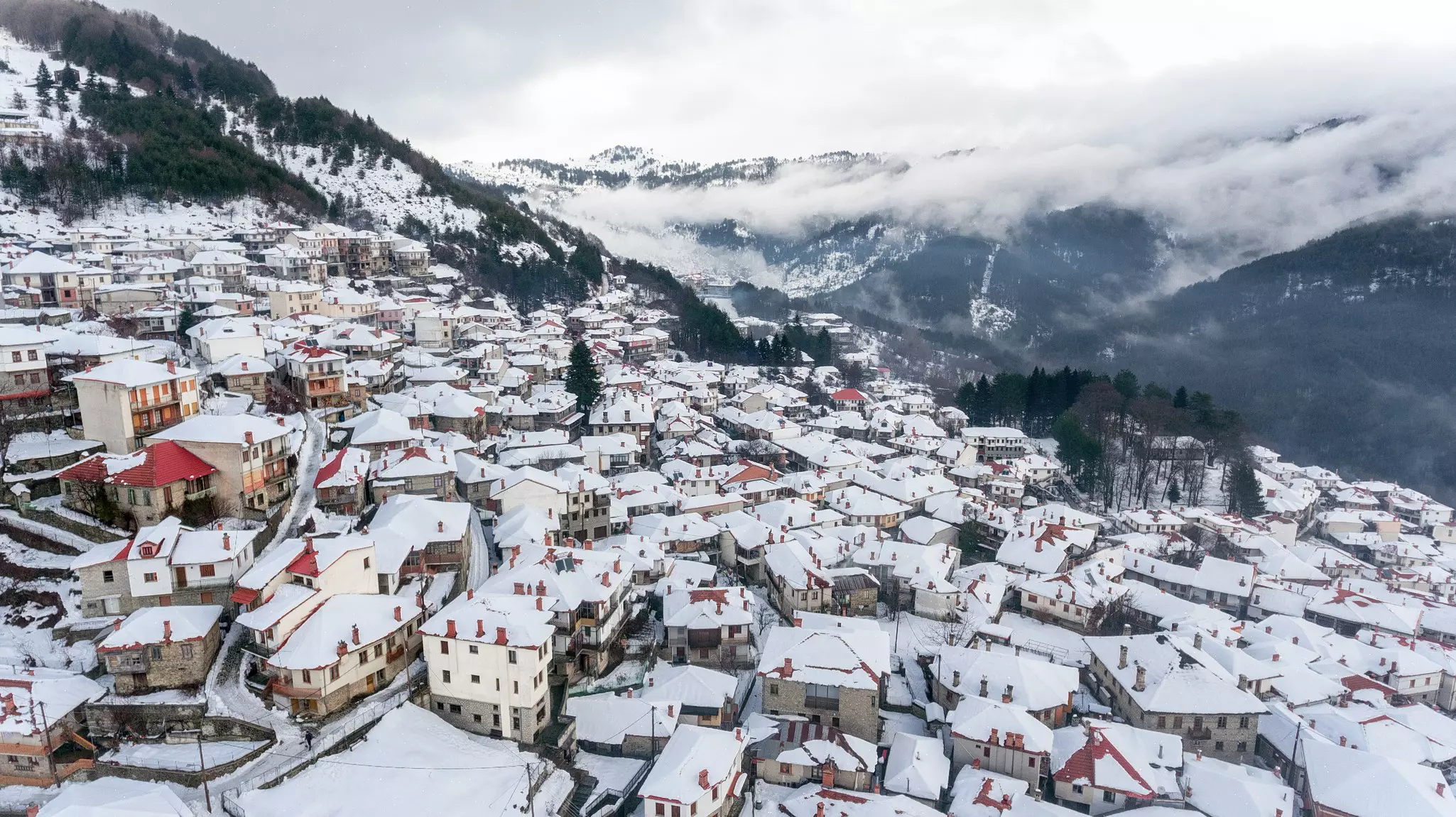 An Alpine-style village on a mountain with cream colored buildings and terracotta rooftops dusted in white snow